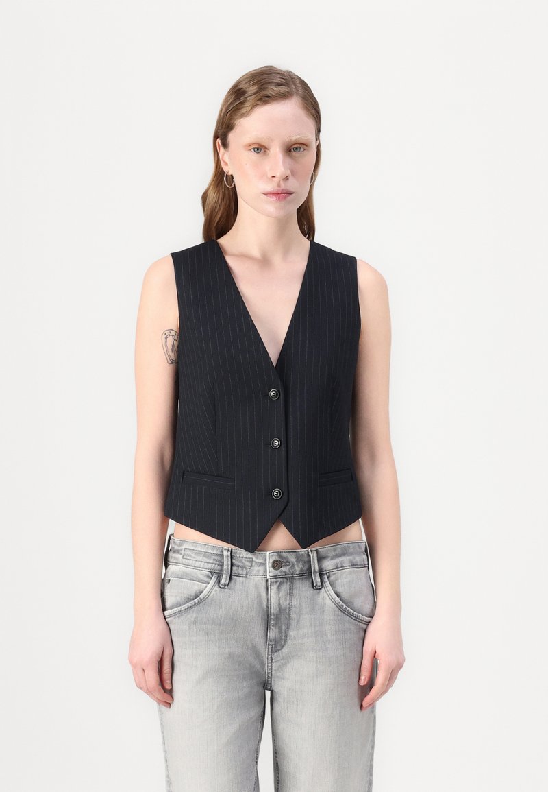 Schwarze Jersey-Weste mit feinen Streifen, tiefem V-Ausschnitt, vierknöpfigem Verschluss und zwei seitlichen Taschen, kombiniert mit grauen Jeans.