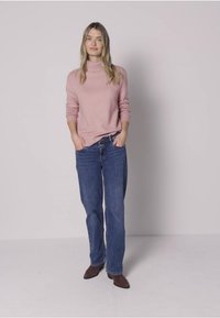 Maglione rosa chiaro a maglia con collo a coste, abbinato a jeans blu larghi e stivaletti marroni, creando un outfit casual.