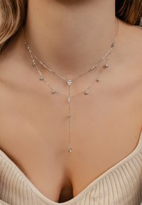 Srebrny naszyjnik warstwowy z różnymi kształtami i akcentami kryształowymi, z centralnym wiszącym wisiorkiem i delikatnym wzorem łańcuszka.