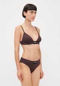 Braunes Bikini-Set mit einem dreieckigen Bralette mit dünnen Trägern und passenden Hipster-Höschen. Beide Teile haben Logo-Details.