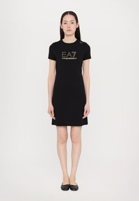 Μαύρο φόρεμα κοντομάνικο με λογότυπο "EA7 Emporio Armani" σε χρυσό. Φτιαγμένο από μαλακό ύφασμα, διαθέτει εφαρμοστή γραμμή και μήκος μέχρι το γόνατο.