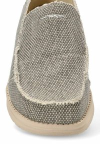 Zapato slip-on tejido gris con un upper de tela texturizada, suela de goma beige y costura visible a lo largo de los bordes. Detalle del logo en la parte frontal.