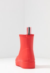 Botte de cheville en caoutchouc rouge avec une finition texturée, dotée d'une languette en tissu rayé à l'arrière et d'un design à bout rond.