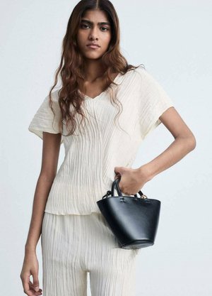Black leather handbag with rounded base and structured handles, paired with a light, pleated cream top, standing against a neutral background.