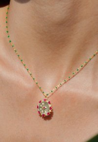 Collier en chaîne dorée avec des perles vertes et un pendentif comprenant un centre texturé en argent entouré d'accents roses.