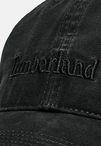 Czarna bawełniana czapka z haftowanym napisem "Timberland". Tekstura jest gładka, z widocznymi detalami przeszyć na daszku.