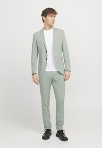 Lys grønn dress med slim fit-design; blazer har spisse revers og lommer; kombinert med en hvit t-skjorte og svarte sko.