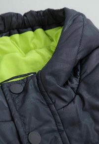 Czarna pikowana kurtka z zielonym wykończeniem, z teksturowanym wzorem i dużymi guzikami do zapięcia. Miękki, ocieplany materiał.