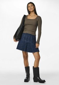 Brązowa prążkowana bluzka z długim rękawem, ciemnoniebieska spódnica w kształcie litery A z surowym wykończeniem oraz czarne, wysokie do kolan botki, zestawione z czarną torbą na ramię.