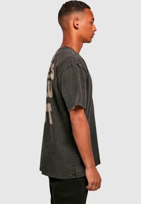 Sort oversized T-shirt med en falmet print, korte ærmer og en løs pasform. Bomuldsstof med en let slidt tekstur.