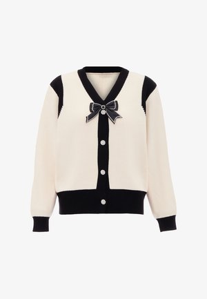 Crème en zwarte geribbelde cardigan met een V-hals, parelachtige knopen en een zwarte strikaccent bij de kraag. Zachte textuur met contrasterende kleuren.