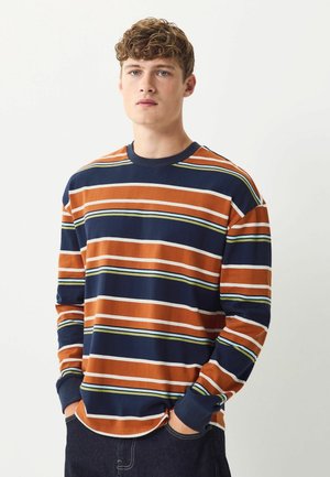 Langærmet stribet skjorte i orange, navy og grøn. Har en rund halsudskæring, kontrasterende manchetter og vandrette striber i varierede bredder.