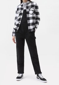 Czarna i biała koszula flanelowa w kratę, czarne ogrodniczki z sztruksu oraz czarne trampki z białą podeszwą. Posiada przednie kieszenie i luźny krój.