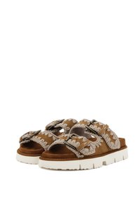 Sandalias de ante marrón con dos correas anchas que cuentan con costuras decorativas en beige y detalles en hebilla de metal, sobre una suela texturizada blanca.