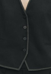 Schwarze Weste mit V-Ausschnitt, sechs schwarzen Knöpfen, weißen Nähten entlang der Kanten und zwei Seitentaschen. Sichtbares strukturiertes Material.