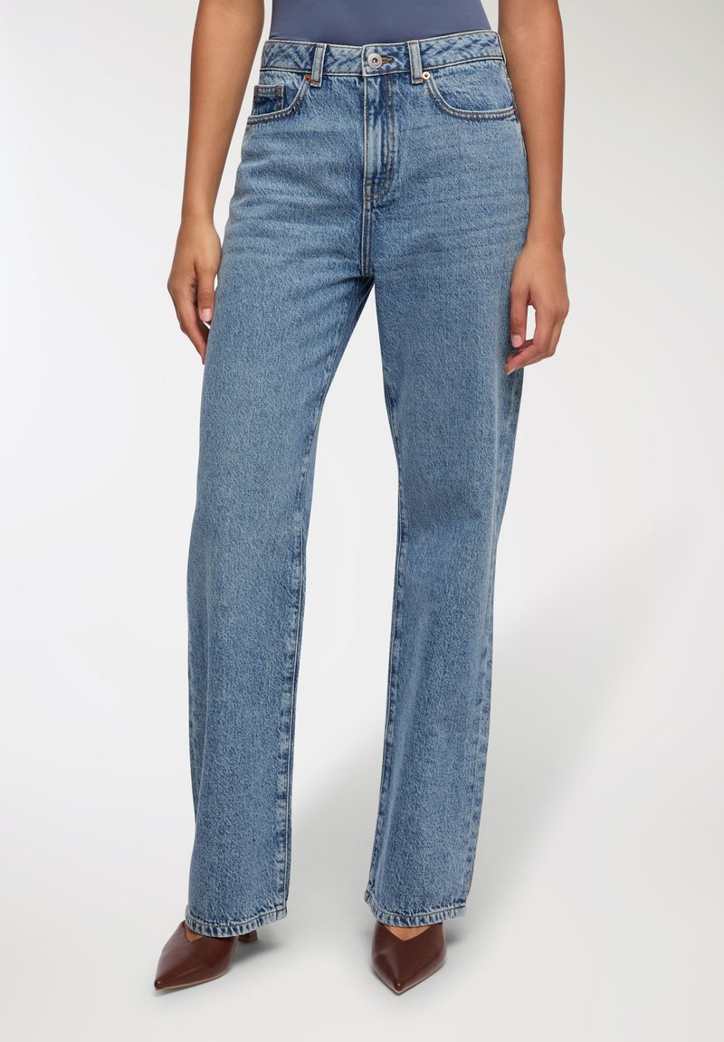 Jasnoniebieskie dżinsy z wysokim stanem o prostym kroju, wykonane z denimu. Zamek błyskawiczny i guzik z przodu, z kieszeniami z przodu i z tyłu.