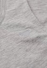 Szara koszulka z dekoltem w serek. Wykonana z miękkiego, teksturowanego materiału. Posiada subtelną, haftowaną wersję logo w lekko ciemniejszym odcieniu szarości.