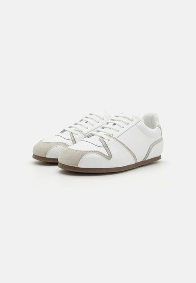 Zapatillas blancas con puntera de ante y acentos laterales. Presentan un diseño cosido y suela de goma. Los cordones son blancos, con una textura suave.