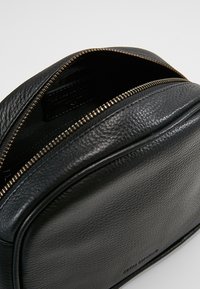 Borsa in pelle nera con finitura testurizzata, dotata di zip superiore e interno liscio. Etichetta visibile all'interno. Forma compatta e arrotondata.