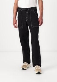 Black pants with contrasting white stitching, straight-leg design, front pockets, and belt loops. Worn with beige sneakers.