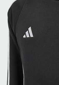 Sweat-shirt noir avec des accents blancs à trois rayures sur les manches et un logo brodé blanc sur la poitrine, fabriqué en tissu doux et texturé.