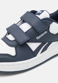 Reebok tenisica s gornjim dijelom od sintetičke kože u tamnoplavoj i bijeloj boji, s Velcro trakama i podstavljenim ovratnikom za udobnost. Bijela guma potplat.