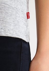 Szara koszulka z materiału z boczną metką z czerwoną marką Levi's, w połączeniu z ciemnymi dżinsami o gładkiej fakturze i dopasowanym kroju.