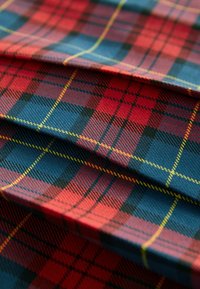 Tissu tartan rouge, bleu et noir avec des lignes jaunes, plié pour montrer la texture en couches et les détails du motif tissé.