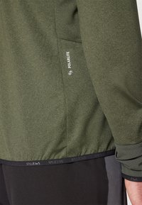 Σκούρο πράσινο σακάκι από ελαστικό υλικό με υφή, που διαθέτει λογότυπο Polarlite και αντίθετο μαύρο ελαστικό στρίφωμα και μανίκια.