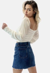Top bianco a maniche lunghe con dettagli arricciati sulla schiena, abbinato a una mini gonna di denim blu con orlo sfrangiato e tasche posteriori.