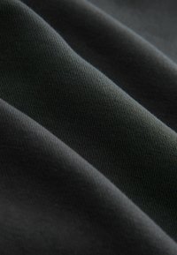 Donkergrijze katoenen stof met een gladde textuur, met een lichte ribbeling en zachte plooien, die de flexibiliteit en val toont.