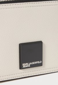 Gray pebbled leather bag featuring a black square logo patch with "KARL LAGERFELD JEANS" text and contrasting stitching along the edges.