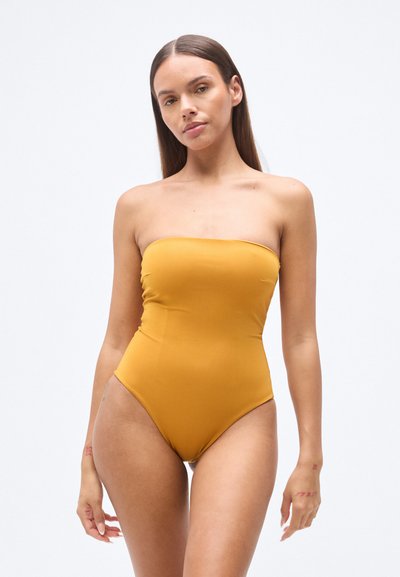 Maillot de bain une pièce jaune moutarde sans bretelles avec une texture lisse et extensible et des jambes échancrées, présentant un design minimaliste sans éléments métalliques ajoutés.
