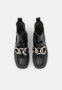 Botines de cuero negro con textura de cocodrilo, detalle de cadena plateada, paneles elásticos en los costados y pespuntes blancos contrastantes en las suelas.