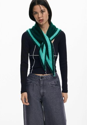 Roheline ja teal kolmnurkne sall, mis on valmistatud pehmest kangast, kantud musta pikakäiselise särgi üle, millel on valge ruuduline muster, ja hallide avarate pükste üle.