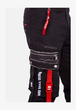 Schwarze Cargo-Hosen mit mehreren Taschen, roten Akzenten, silbernen Nieten und strukturierten Reißverschlüssen. Mit Markenlogo und verstellbaren Trägern.