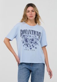 T-shirt di cotone azzurro chiaro con una grafica floreale e il testo "ROMANTICIZE YOUR LIFE" in caratteri bold sulla parte anteriore. Maniche corte, vestibilità comoda.