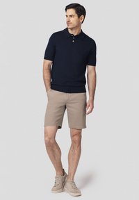 Granatowa koszulka polo z krótkim rękawem i trzema guzikami, w zestawieniu z beżowymi bawełnianymi szortami oraz jasnobrązowymi trampkami. Casualowy i dopasowany krój.
