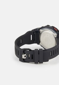 Bracelet de montre de sport en caoutchouc noir avec une surface texturée, une boucle ajustable et des découpes visibles pour la respirabilité. Panneau arrière argenté.