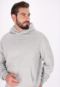 Grå huvtröja med framficka, bekväm textur, ribbade muddarna och en diskret broderad logotyp på bröstet. Slät fleece-material.