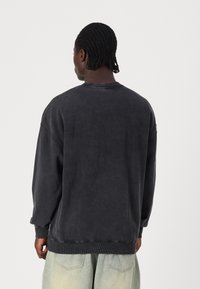 Oversized dark gray sweatshirt with ribbed cuffs and hem, featuring a crew neckline and soft, textured fabric. Minimalistic design with no patterns.