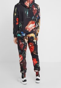 Svart hoodie- och sweatpants-set med blommönster, med livliga rosor och andra blommor. Inkluderar dragkedjor vid byxbenen och en huva.