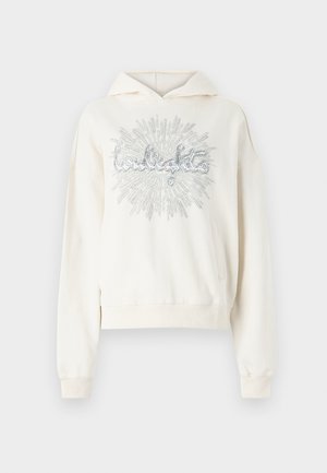 Hoodie couleur crème en tissu doux, avec une inscription en paillettes argentées au centre et une poche frontale.