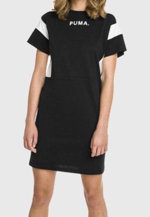 Mujer con un vestido corto de manga corta de Puma en blanco y negro, con el logo en el pecho, de pie con los brazos relajados a los lados.