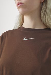 Braunes Baumwoll-T-Shirt mit kurzen Ärmeln, das ein helles Nike-Logo auf der Brust, einen runden Ausschnitt und eine glatte Textur aufweist.