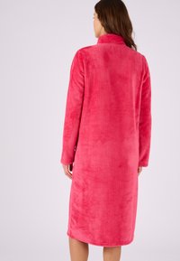 Accappatoio in pile rosa con tessuto texturizzato, maniche lunghe e colletto alto, che arriva fino a metà polpaccio. Aspetto morbido e accogliente.