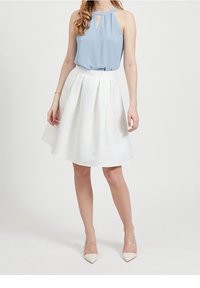 Světle modrý halter top s detaily klíčové díry v kombinaci s bílou rozšiřující se sukní. Průhledné podpatky doplňují outfit. Hladká textilie.