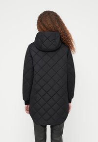 Μαύρο καπιτονέ μπουφάν με κουκούλα, με διακοσμητικό σχέδιο σε σχήμα διαμαντιού, μακριά μανίκια και ριμπ μανσέτες. Το υλικό φαίνεται λείο και ελαφρύ.