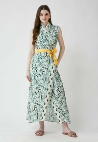 Zaļš un krēmkrāsas maksi kleita ar abstraktiem lapu rakstiem, ar sānu apkakli, bez piedurknēm un dzeltenu jostu viduklī. Teksturēts audums ar maigu apdari.