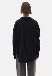 Donkerblauwe blouse, losse pasvorm, lange mouwen, detail met rugplooien, kraag, gecombineerd met lichtgrijze gestructureerde broek. Strak, minimalistisch ontwerp.